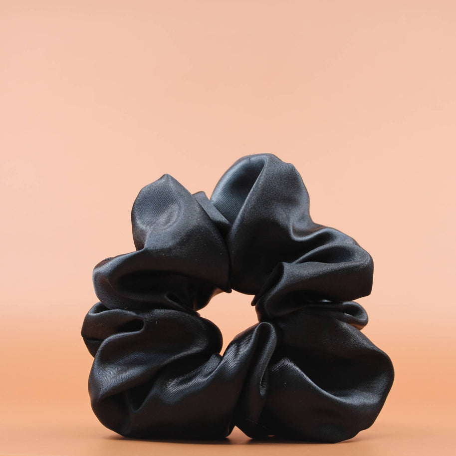 Afro Scrunchie Satin Schwarz Vorderansicht vor einem braunen Hintergrund