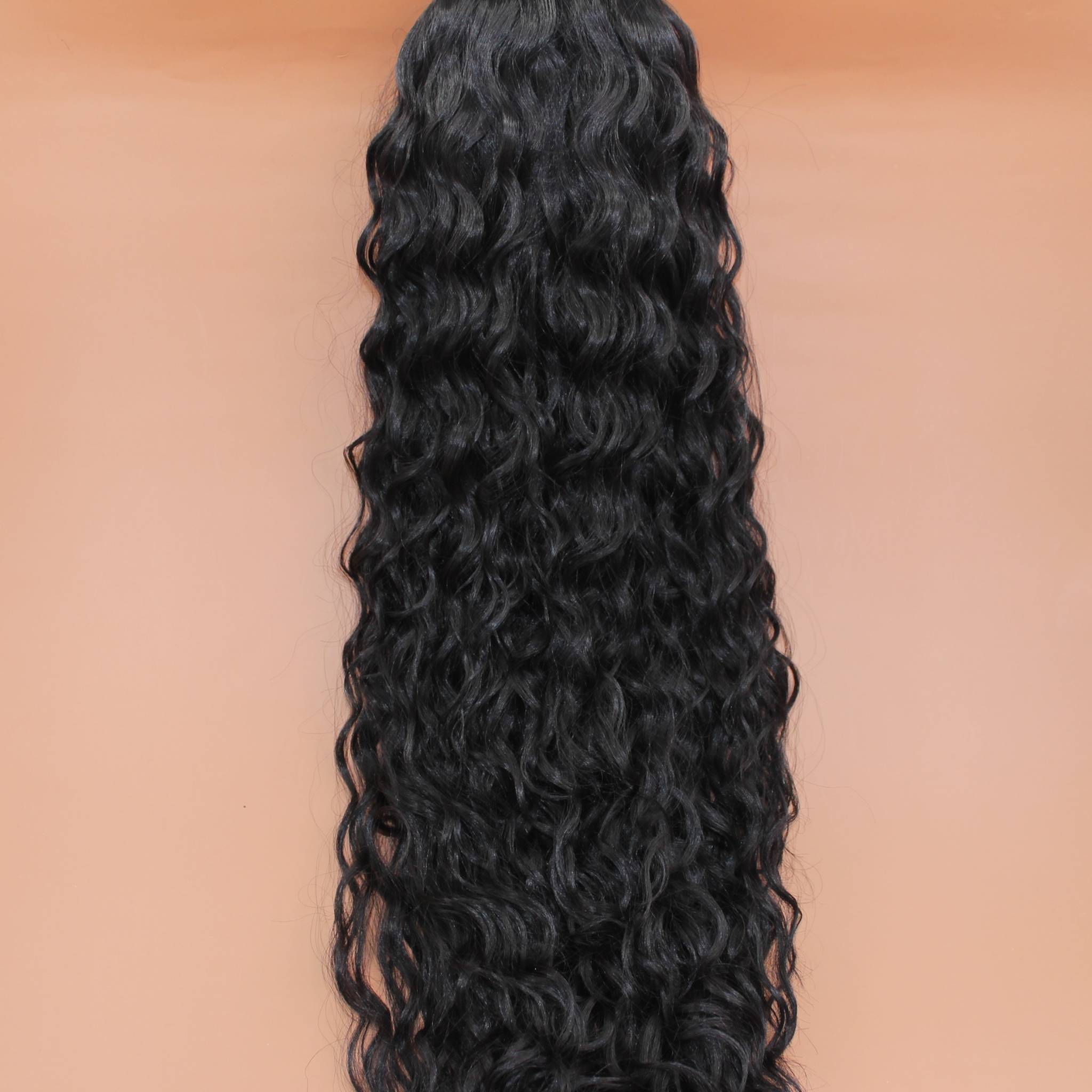 DREAM HAIR Ponytail Diborra Curly, Farbe 2 (dunkelbraun) in der Vorderansicht vor einem braun-orangen Hintergrund.