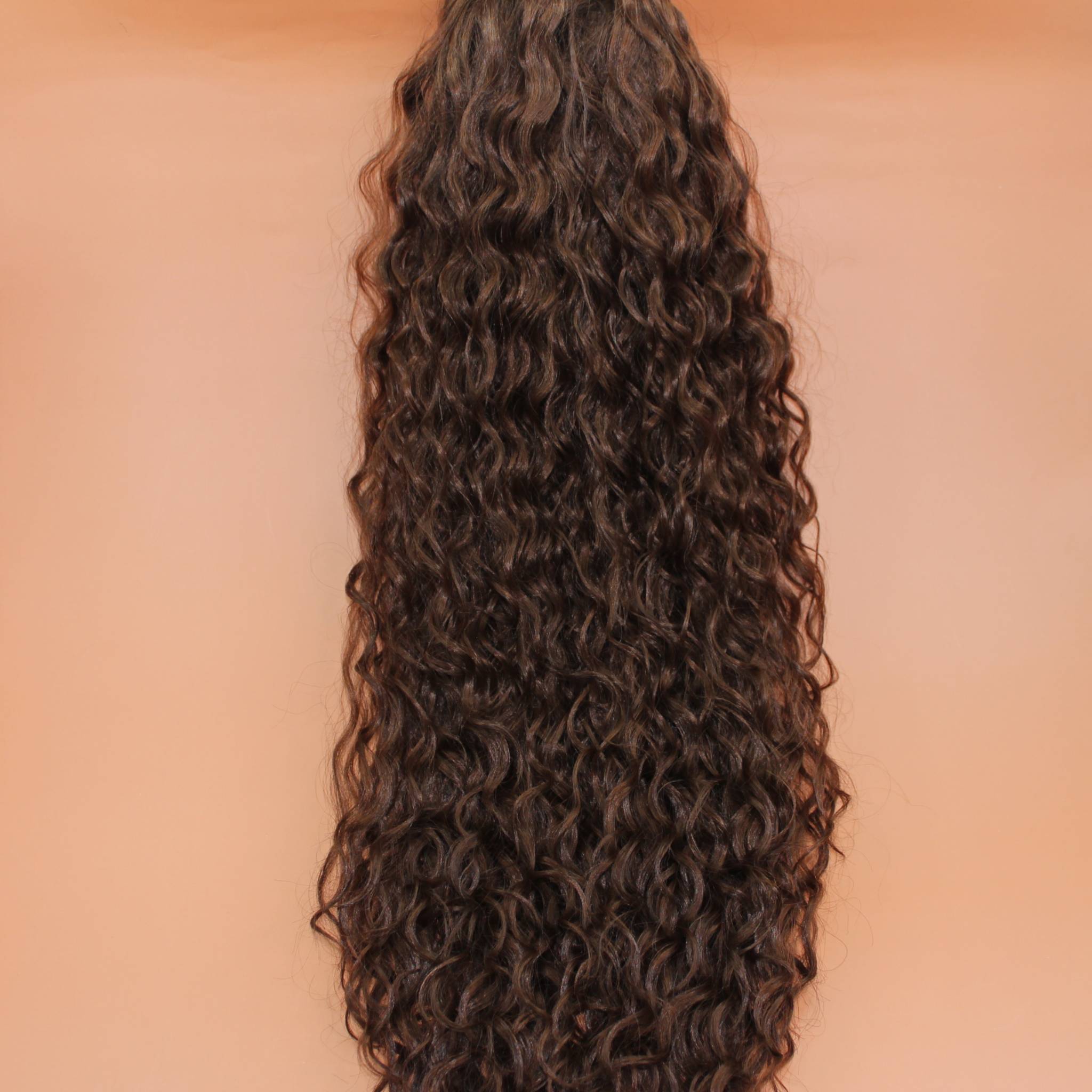 DREAM HAIR Ponytail Diborra Curly, Farbe 6 (mittelbraun) in der Vorderansicht vor einem braun-orangen Hintergrund.