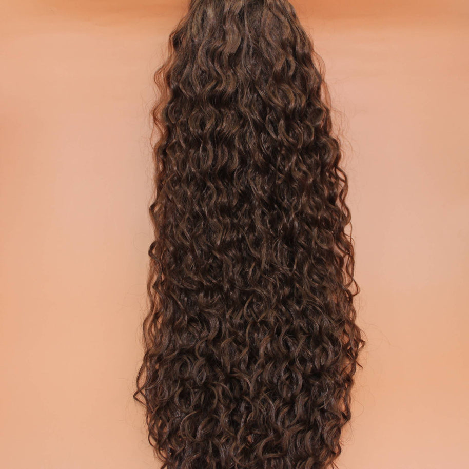 DREAM HAIR Ponytail Diborra Curly, Farbe 6 (mittelbraun) in der Vorderansicht vor einem braun-orangen Hintergrund.