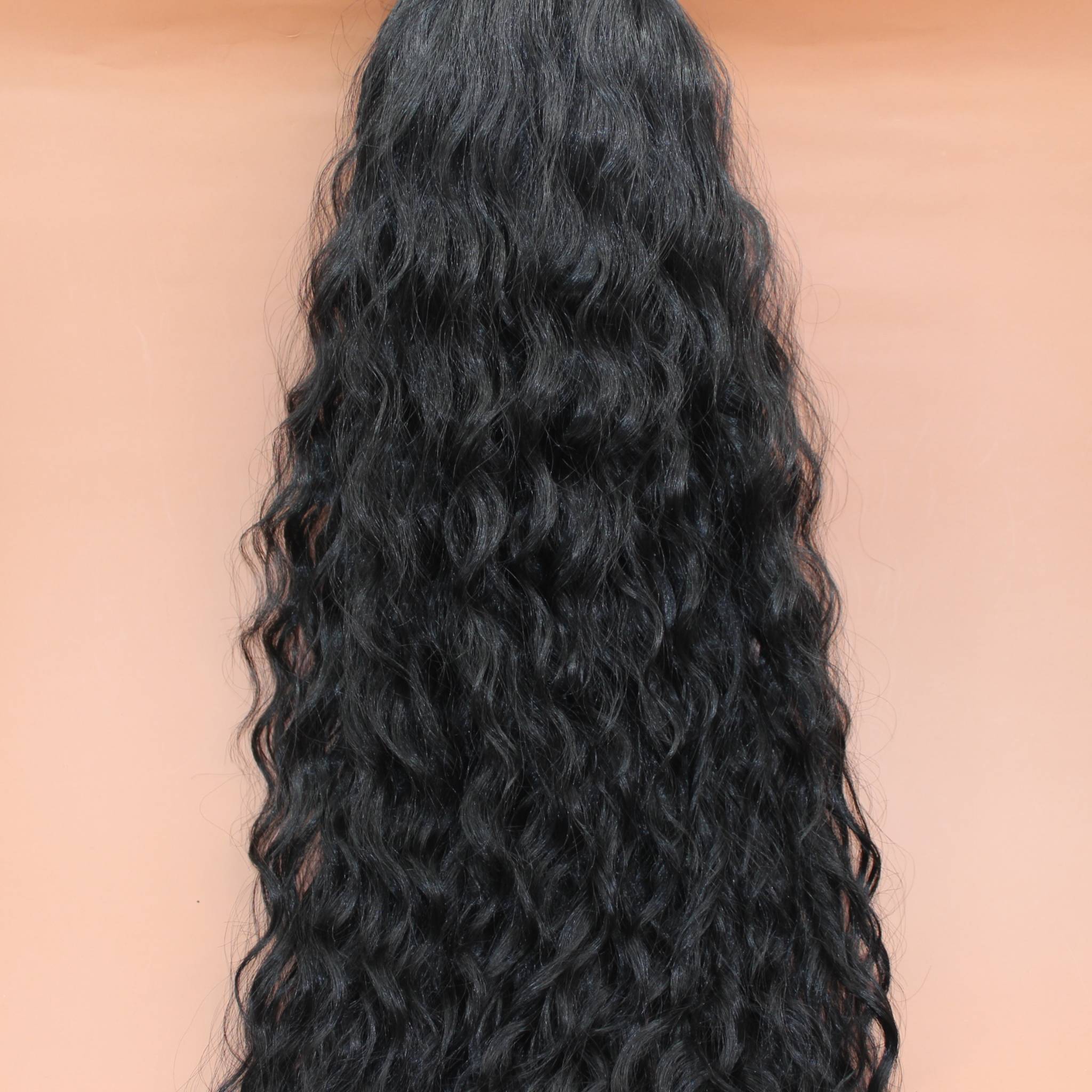 DREAM HAIR Ponytail Diborra Curly, Farbe 1B (schwarz) in der Vorderansicht vor einem braun-orangen Hintergrund.