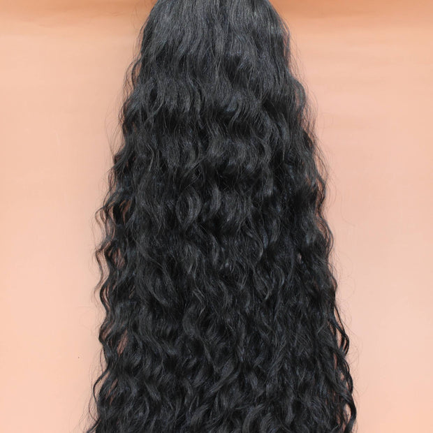 DREAM HAIR Ponytail Diborra Curly, Farbe 1B (schwarz) in der Vorderansicht vor einem braun-orangen Hintergrund.