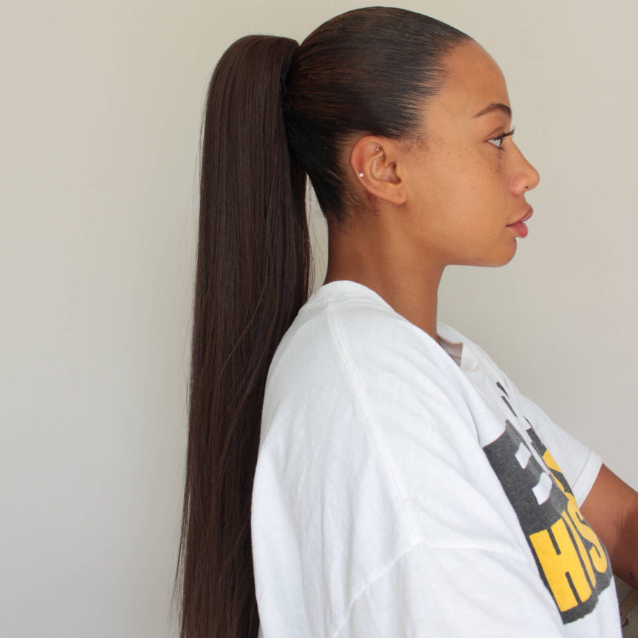 Junge Frau trägt den DREAM HAIR Ponytail Straight 30 inches in der Seitenansicht vor einem hell-grauen Hintergrund.