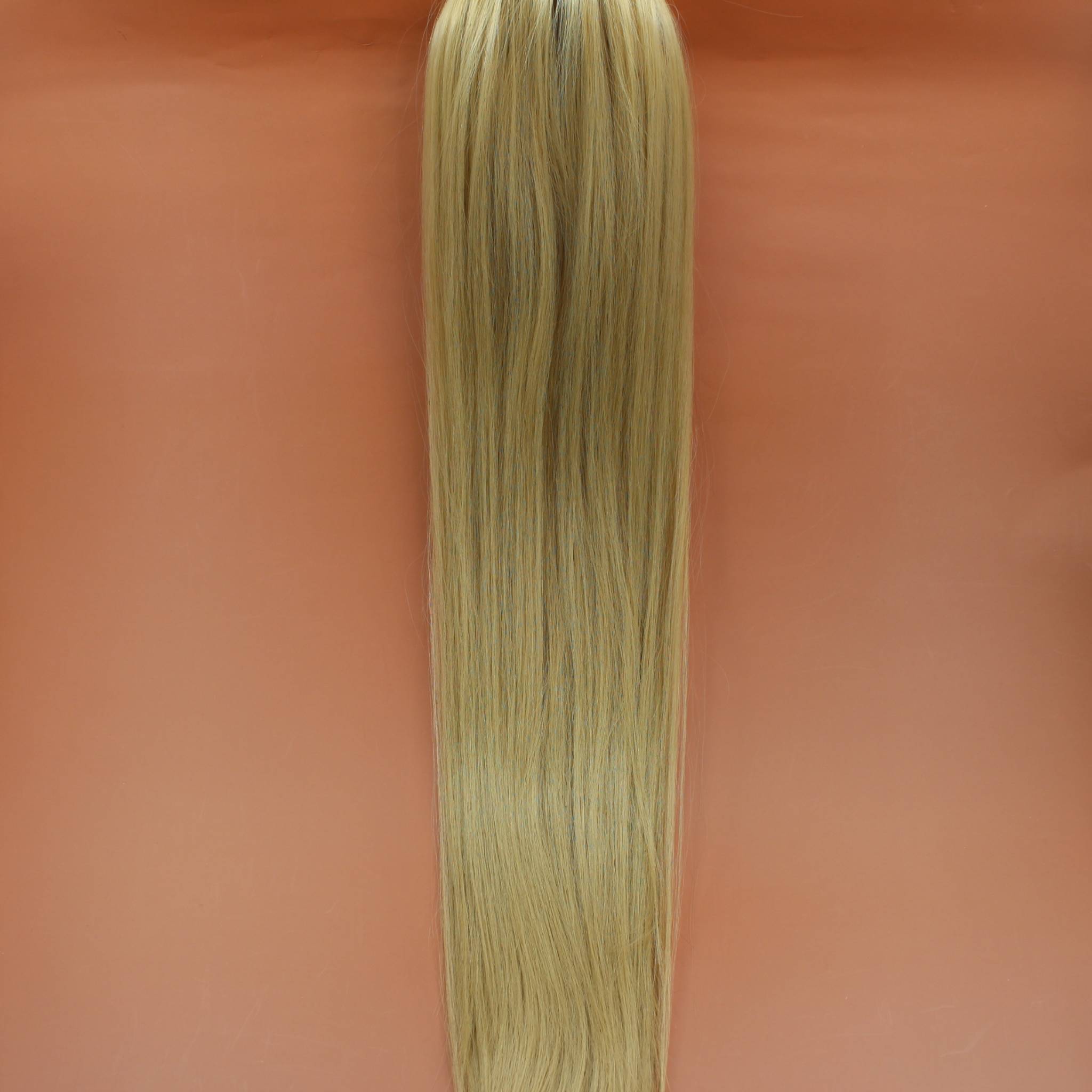DREAM HAIR Ponytail Straight 30'', Farbe 22 (blond) in der Vorderansicht vor einem braun-orangen Hintergrund.