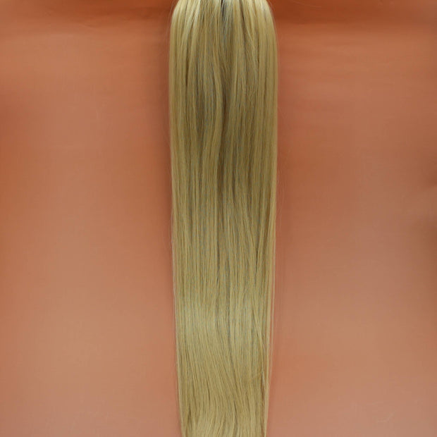 DREAM HAIR Ponytail Straight 30'', Farbe 22 (blond) in der Vorderansicht vor einem braun-orangen Hintergrund.