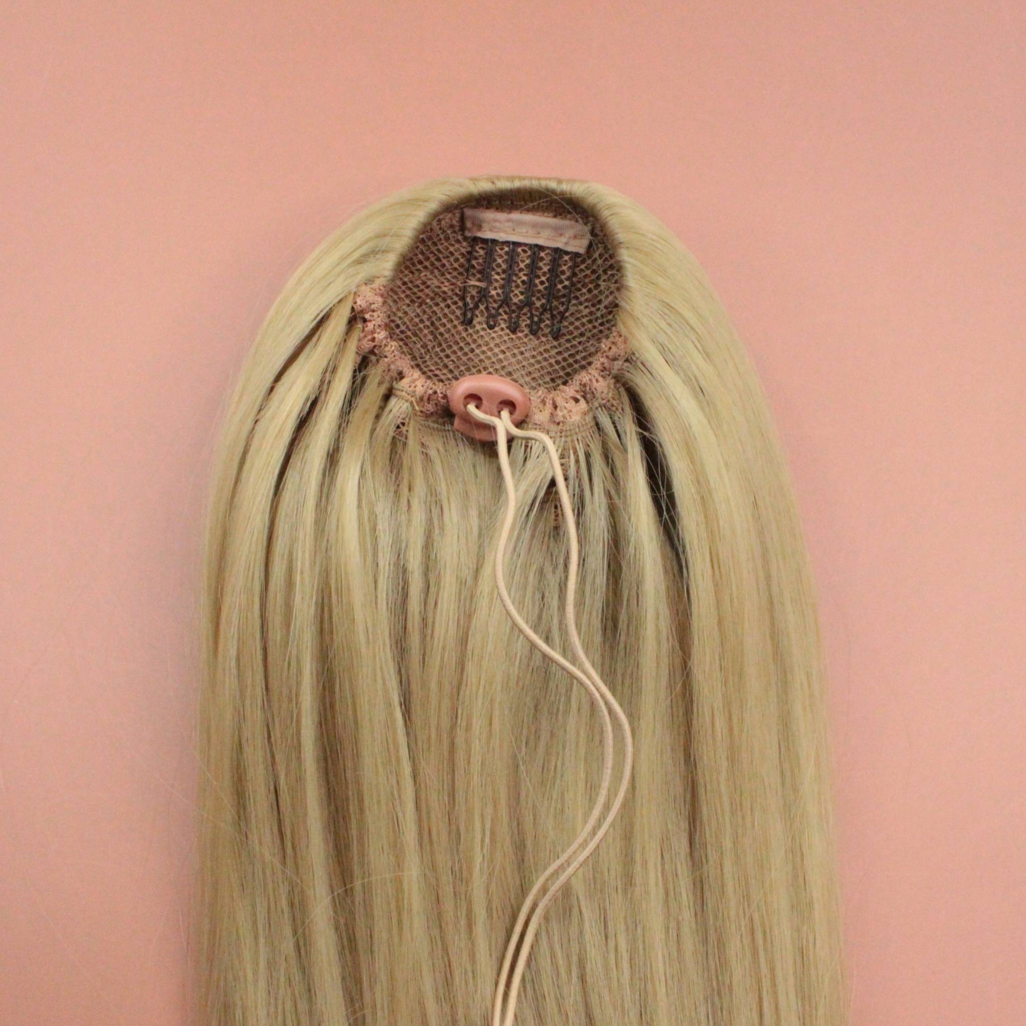 DREAM HAIR Ponytail Straight 30'', Farbe 22 (blond) in der Rückansicht vor einem braun-orangen Hintergrund.