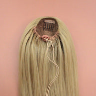 DREAM HAIR Ponytail Straight 30'', Farbe 22 (blond) in der Rückansicht vor einem braun-orangen Hintergrund.