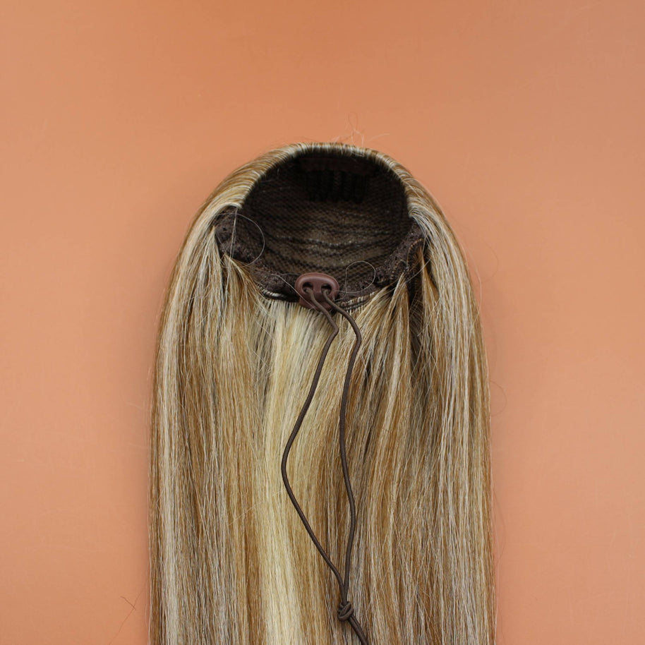 DREAM HAIR Ponytail Straight 30'', Farbe 18/22 (blond mix) in der Rückansicht vor einem braun-orangen Hintergrund.