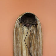 DREAM HAIR Ponytail Straight 30'', Farbe 18/22 (blond mix) in der Rückansicht vor einem braun-orangen Hintergrund.