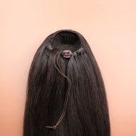 DREAM HAIR Ponytail Straight 30'', Farbe 4 (braun) in der Rückansicht vor einem braun-orangen Hintergrund.