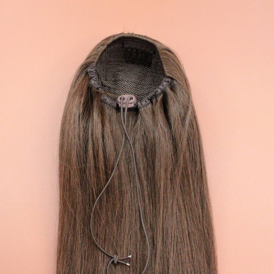 DREAM HAIR Ponytail Straight 30'', Farbe 8 (mittelbraun) in der Rückansicht vor einem braun-orangen Hintergrund.