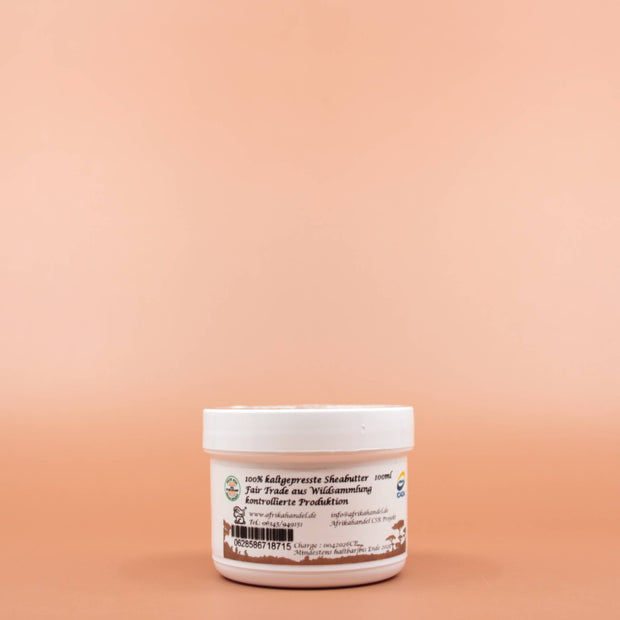 SHEA GOLD 100% Natural Fair Trade Bio Sheabutter 100ml in der Vorderansicht vor einem braun-orangen Hintergrund.