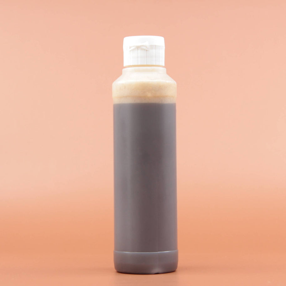Das Hautpflegeprodukt SHEA GOLD Liquid Black Soap 240ml in der Rückansicht vor einem braun-orangen Hintergrund.