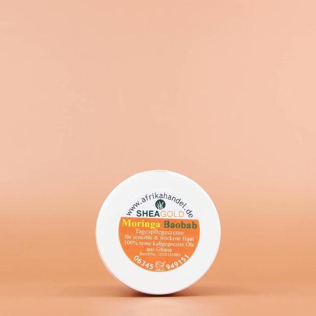 SHEA GOLD Moringa Baobab Sheabutter Creme 100ml Ansicht vom Deckel vor einem orange braunen Hintergrund 