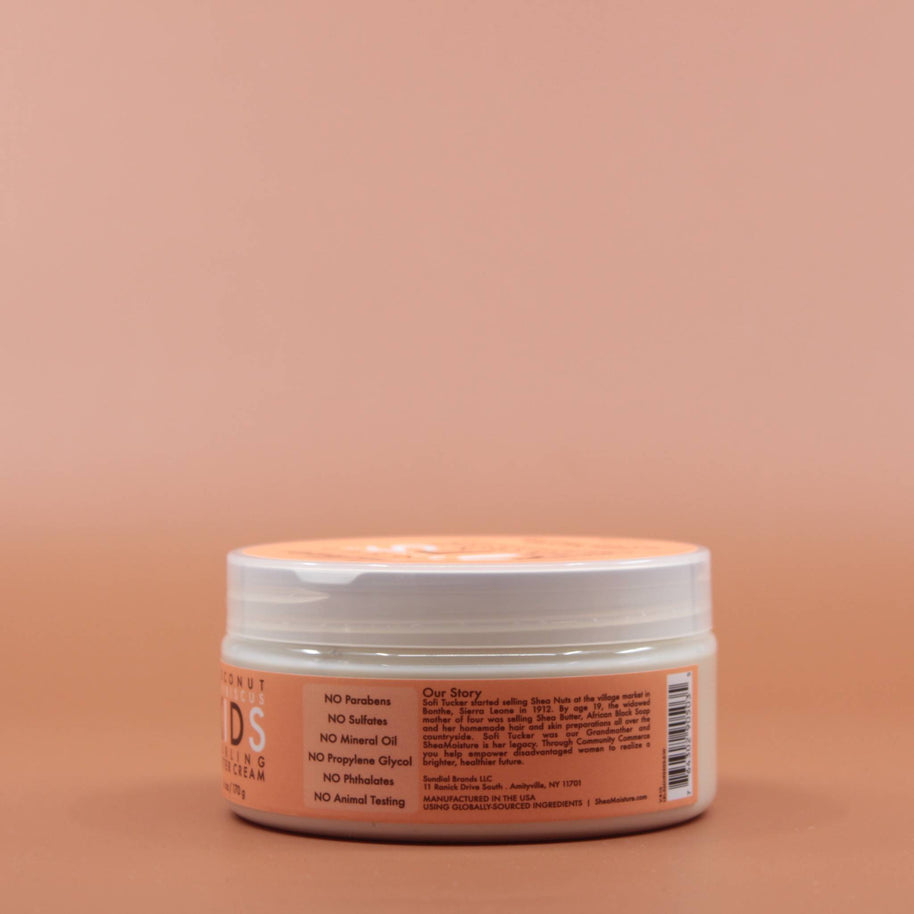 Das Kinder Haarpflegeprodukt SHEA MOISTURE Kids Curling Butter Cream 170g in der Seitenansicht (links) vor einem braun-orangen Hintergrund.